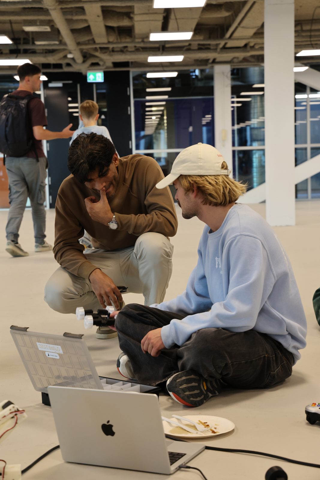 Gustav cross-legged on the floor with a builder, laptop and board between them