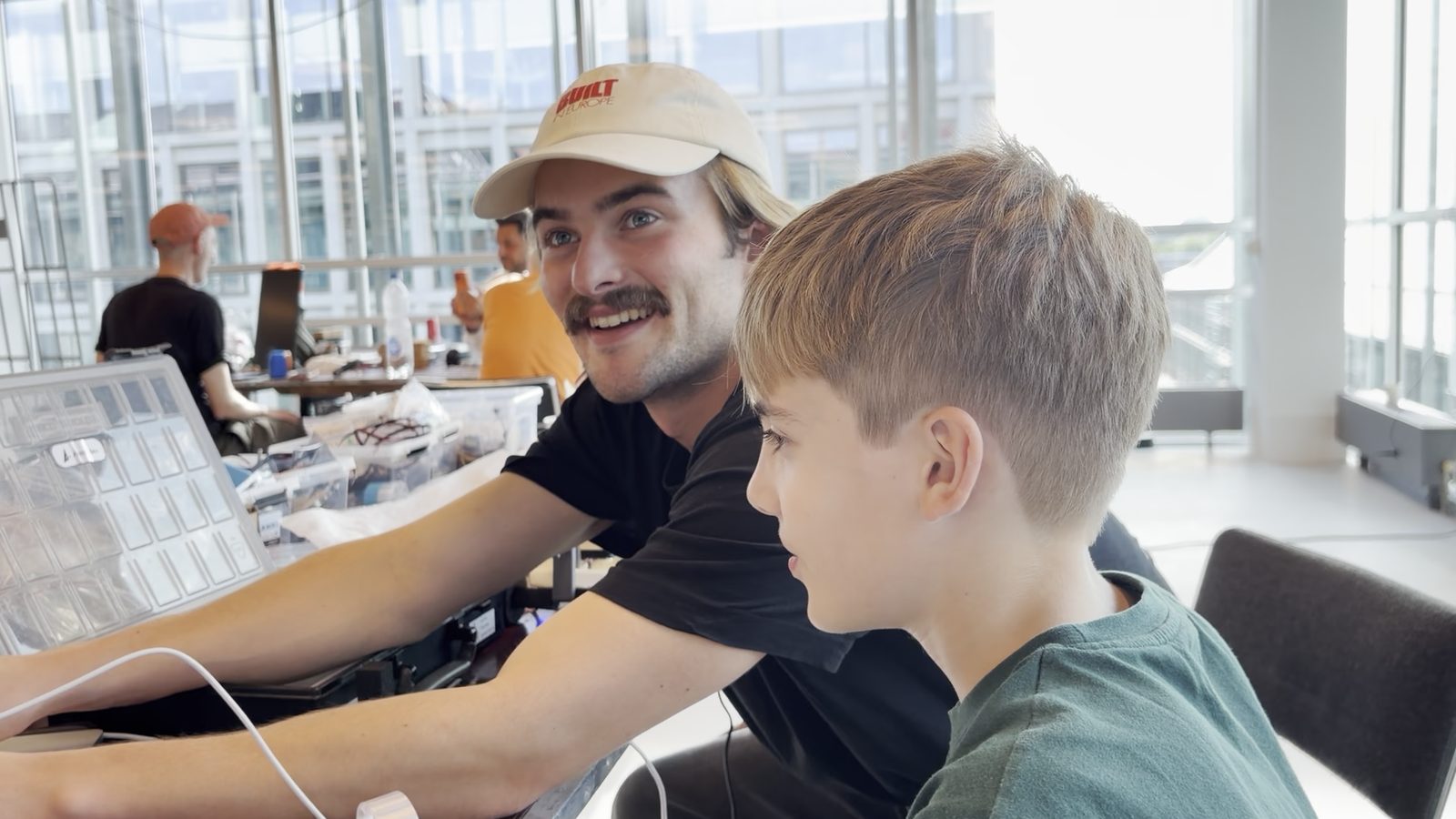 Gustav and a boy at the table by the window, looking at the screen together