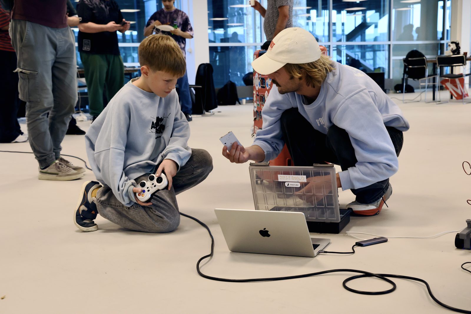 A boy with a gamepad and Gustav kneeling by the laptop and the robot car