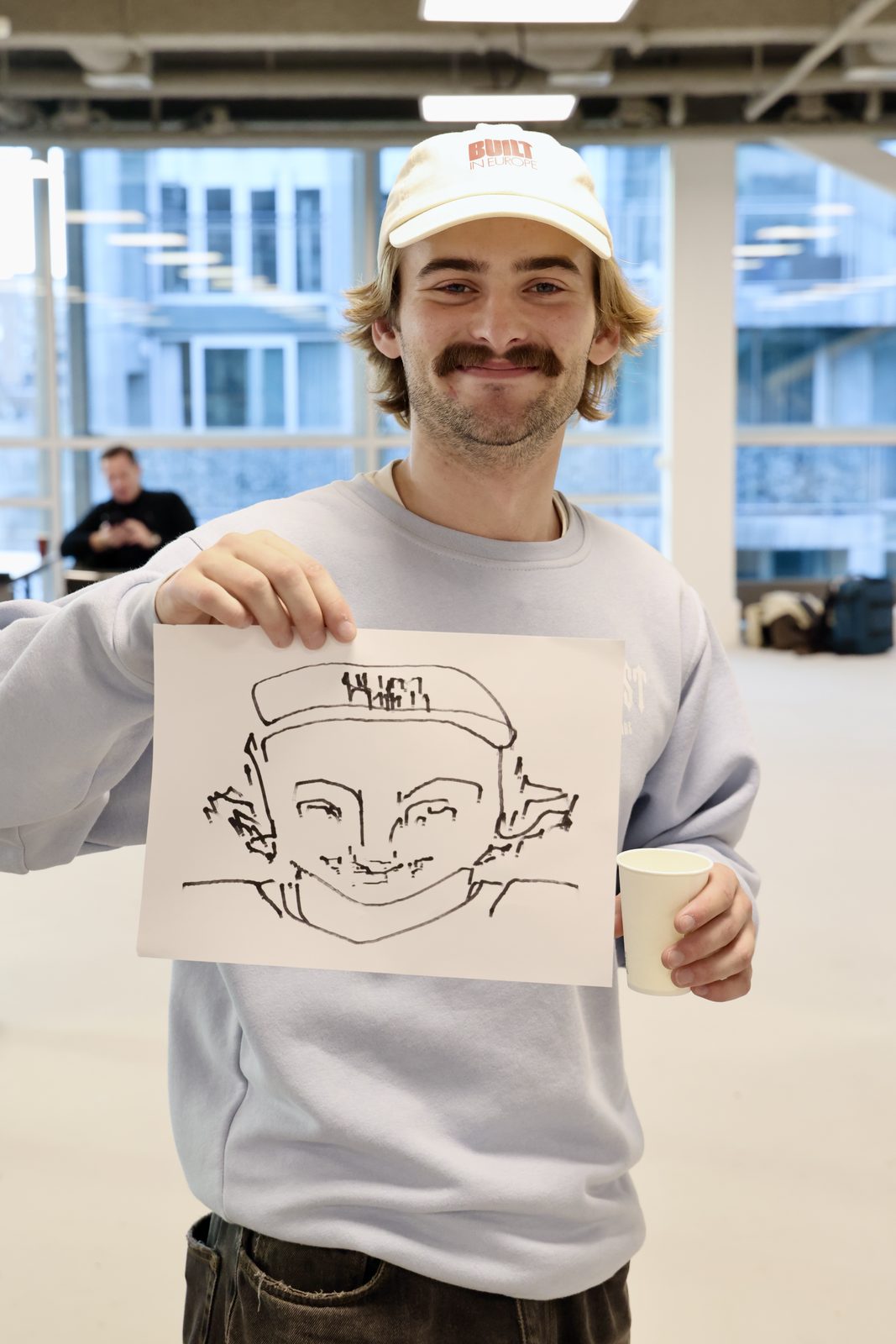 Gustav holding up the portrait a robot arm drew of him