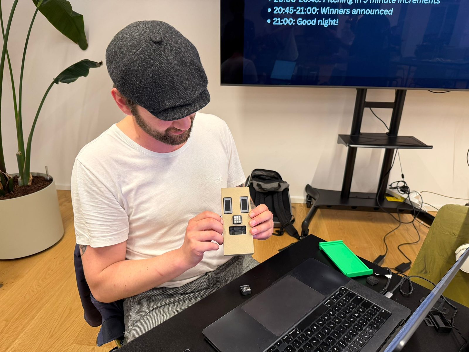 A builder in a flat cap holding up a cardboard prototype with two small screens