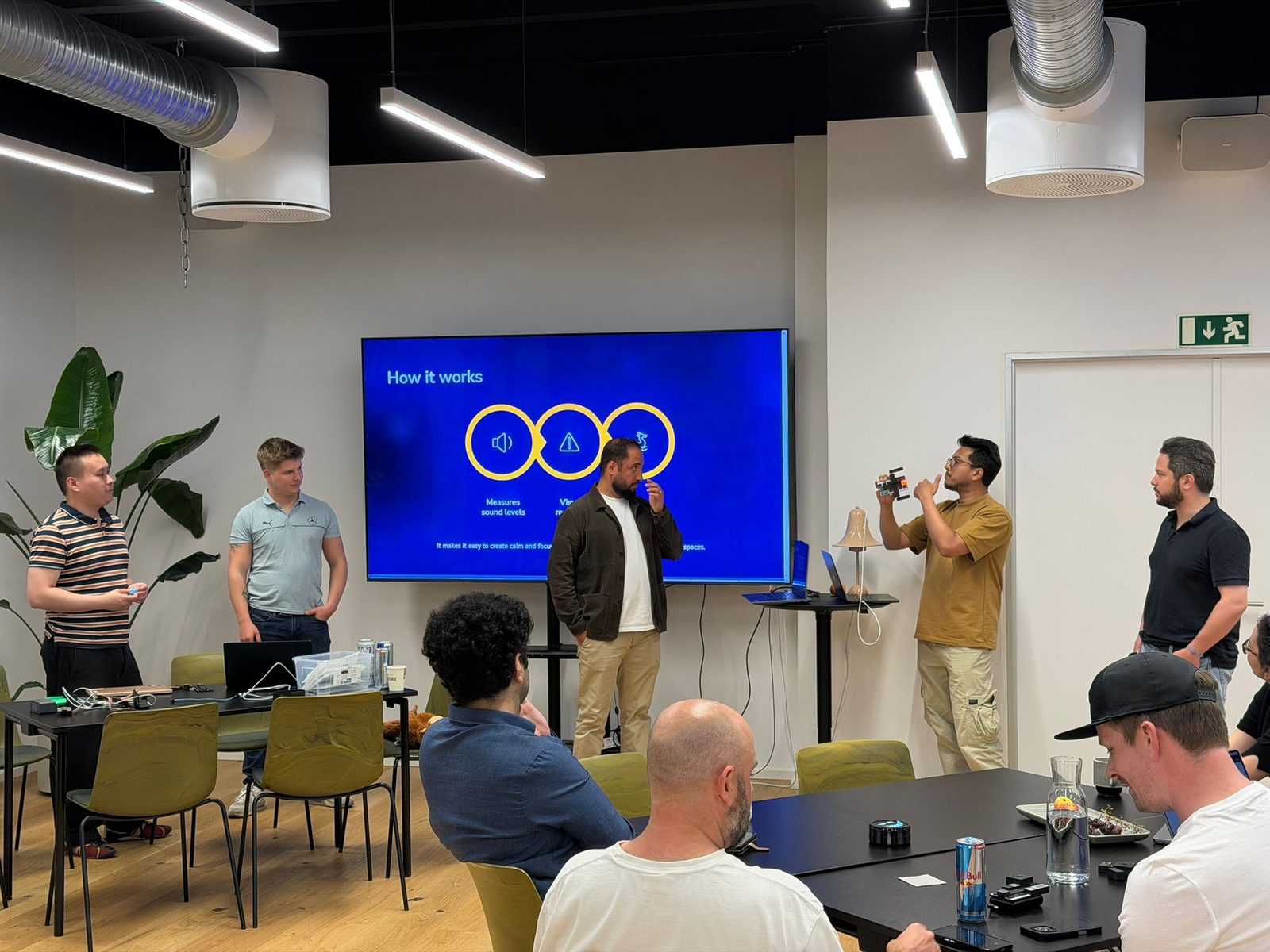 A team pitching in front of a blue how-it-works slide while the audience films