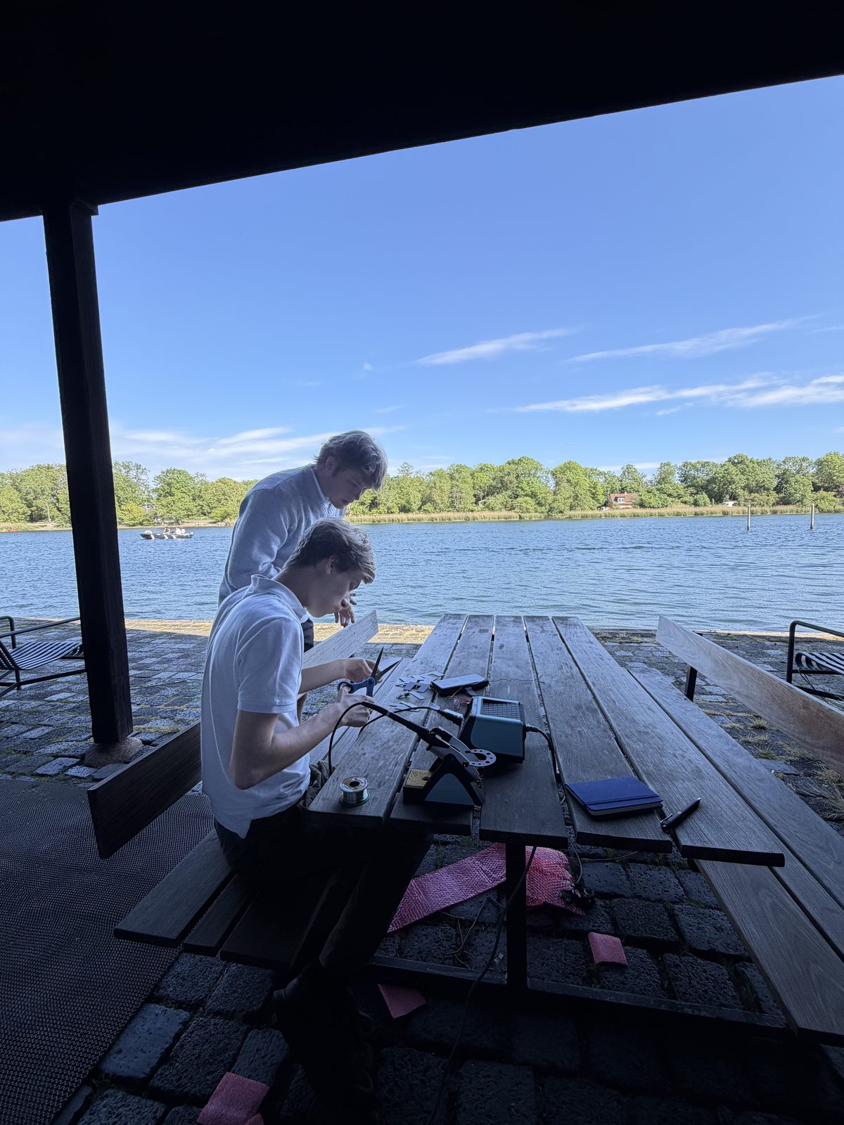 Two builders assembling a device at a lakeside picnic table