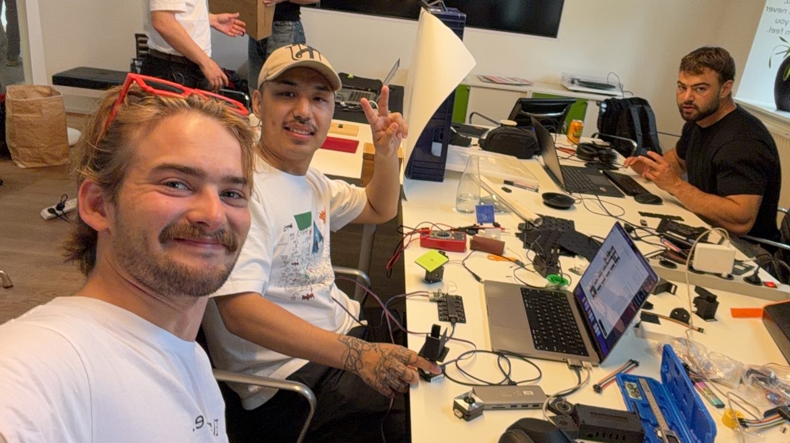 Gustav with two builders at a desk full of robot arm parts and laptops