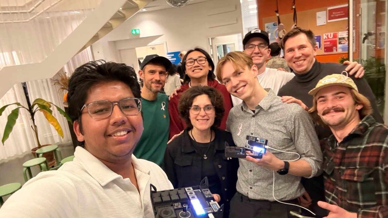 Six builders and Gustav in a selfie, one holding a lit-up board