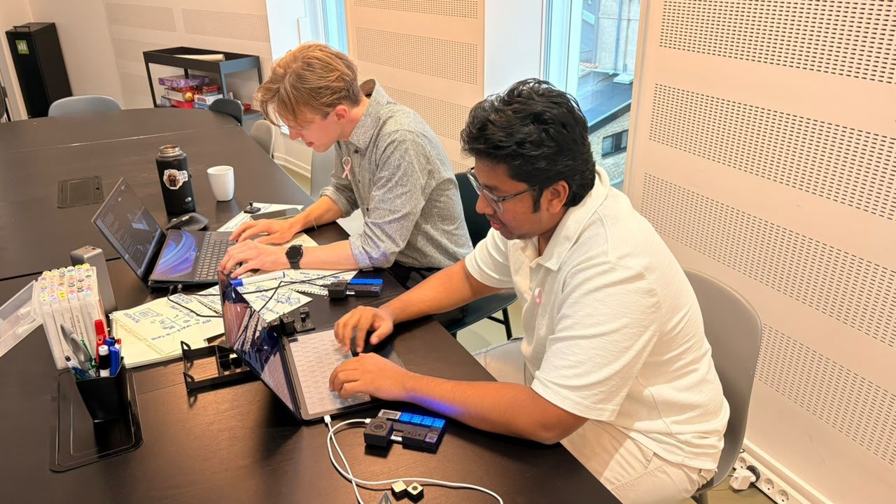 Two builders at a table with the board plugged into a laptop