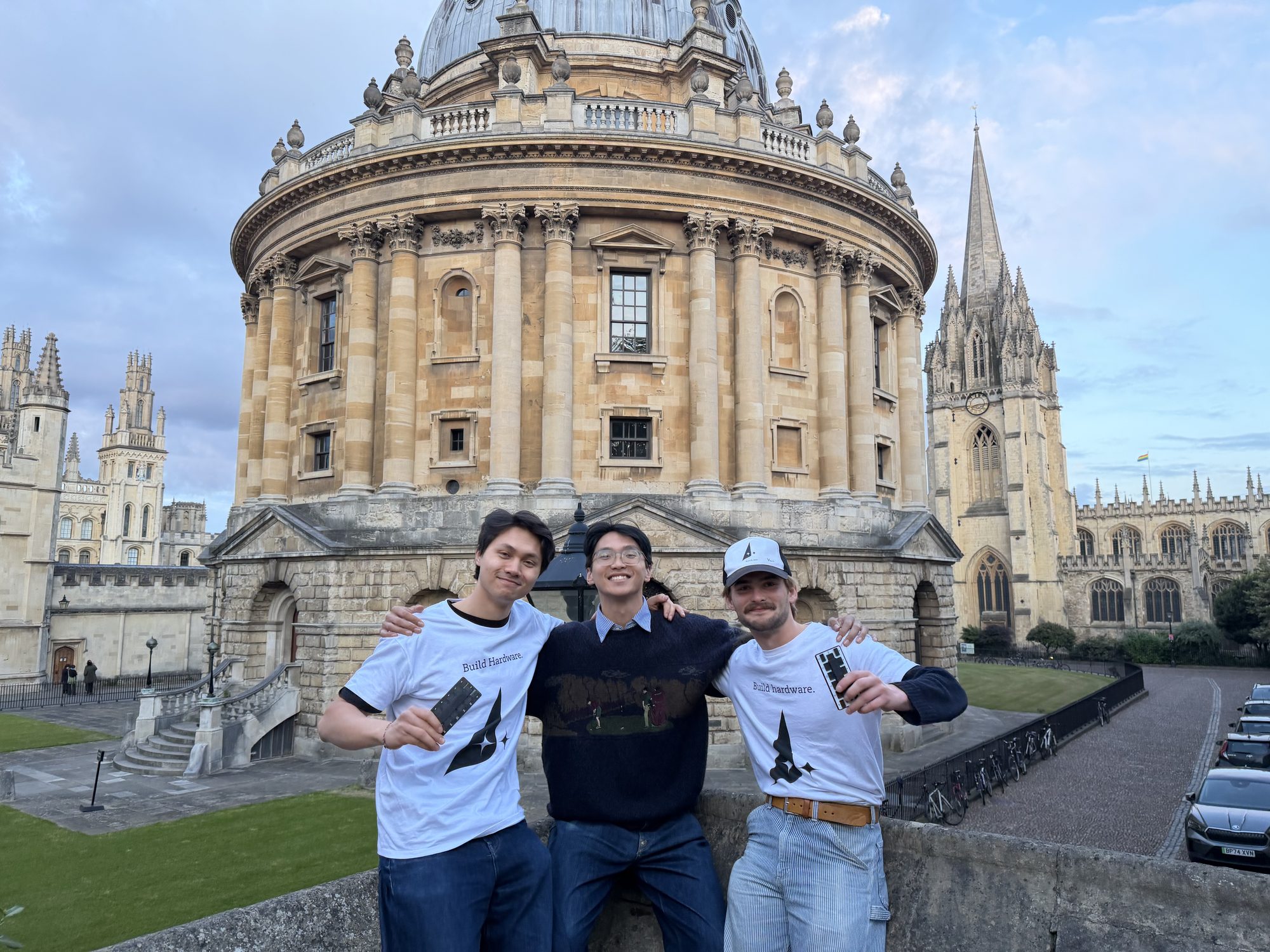 Three builders in Build Hardware shirts holding Atech boards in front of the Radcliffe Camera, Oxford, evening light